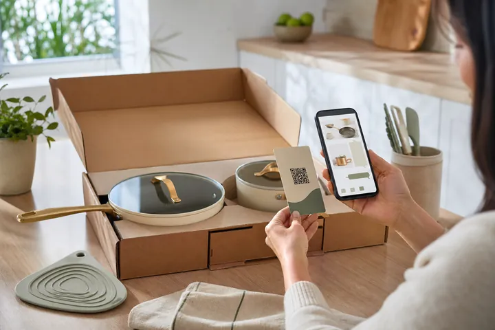 A customer scanning a QR insert while unboxing cookware and opening a product catalog on a phone